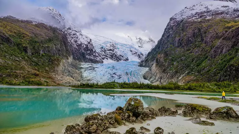 Adventurist exploring the glaciers of Patagonia next to teal water and steep green mountains