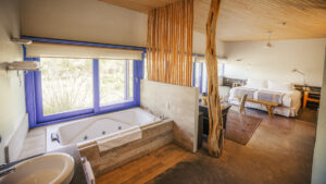 Large room of Catur Suite with bed, loveseat, table & chairs, jetted bathtub & large windows at Explora Atacama Lodge in Chile.
