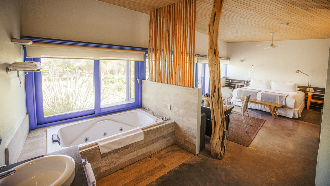Large room of Catur Suite with bed, loveseat, table & chairs, jetted bathtub & large windows at Explora Atacama Lodge in Chile.
