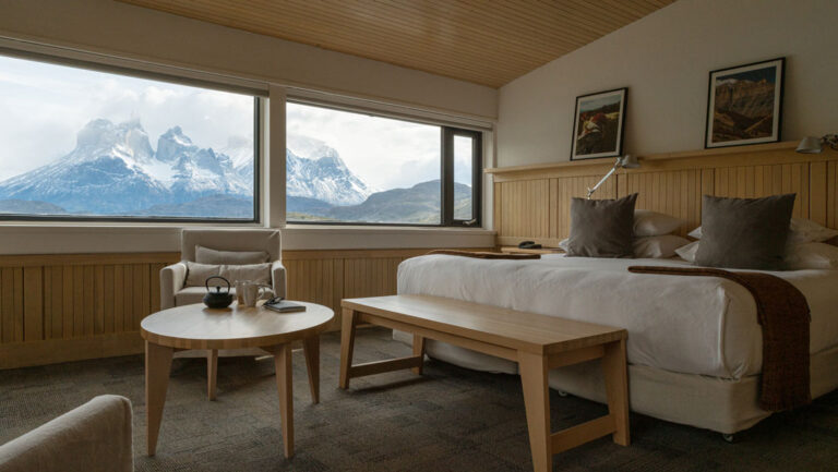 Large bed, table, two chairs, views to water and mountains from Exploradores Suite at Explora Torres del Paine Lodge in Chile.