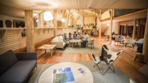 Living area at Explora Sacred Valley Lodge with high ceilings, various wood touches & seating areas, one with guests eating.