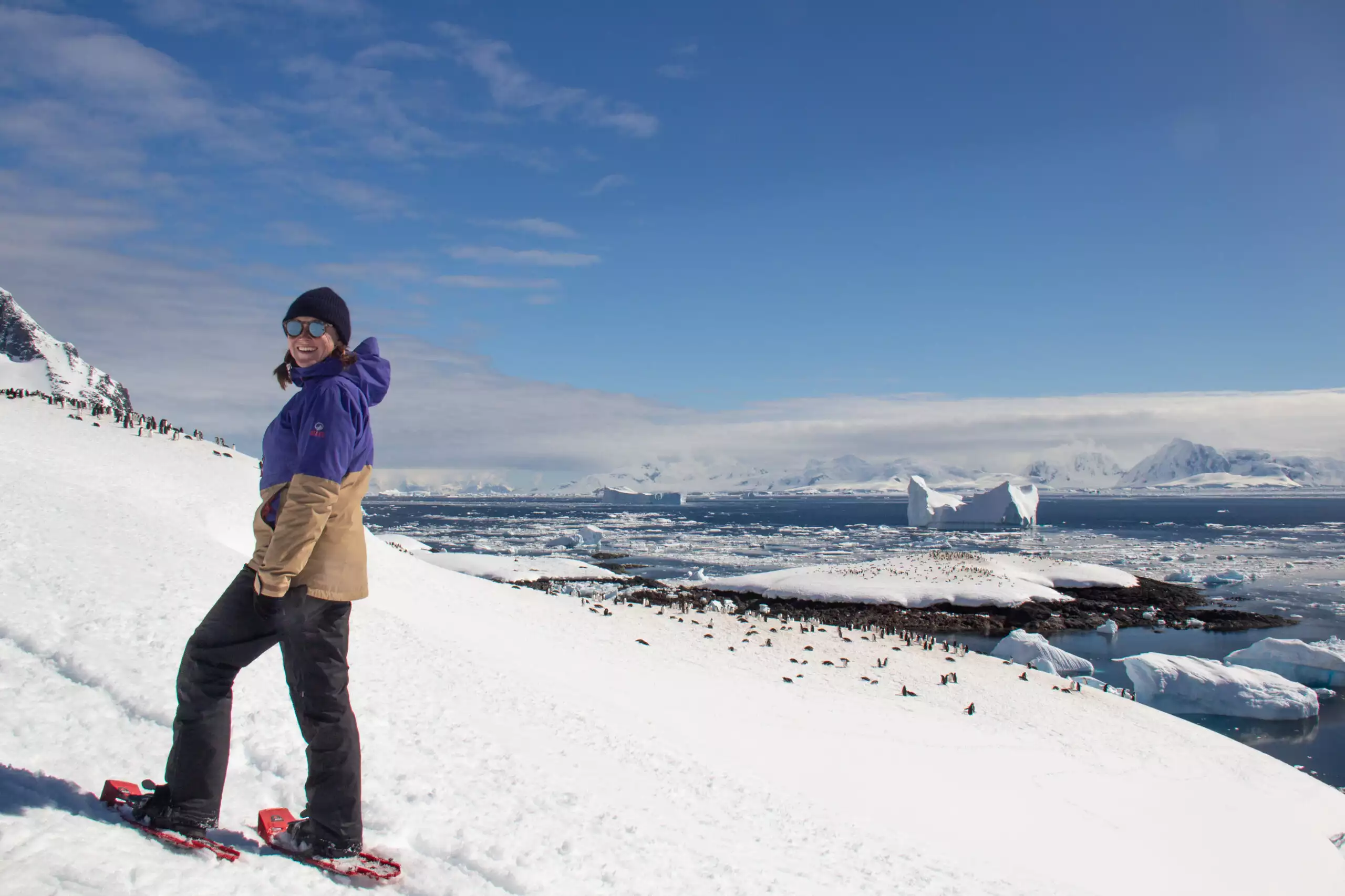 Women snowshoing though the Antarctica hills looking down on a colony of penguins