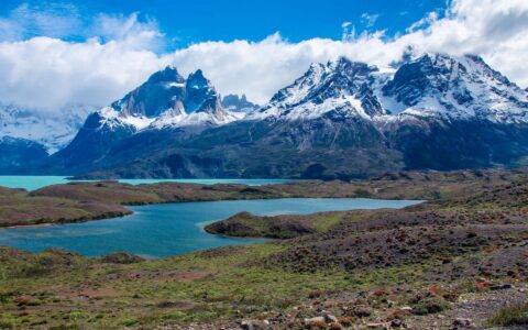 Snowy mountains overlooking teal waterways of Patagonia with blue skys and bright white clouds