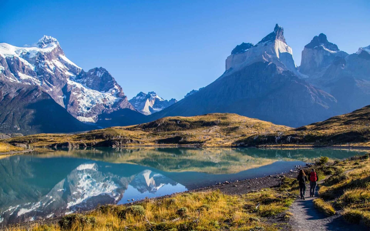 hikers walking toward a lake in Torres Del Paine on a sunny day with jagged mountains in the background during a patagonia tour.