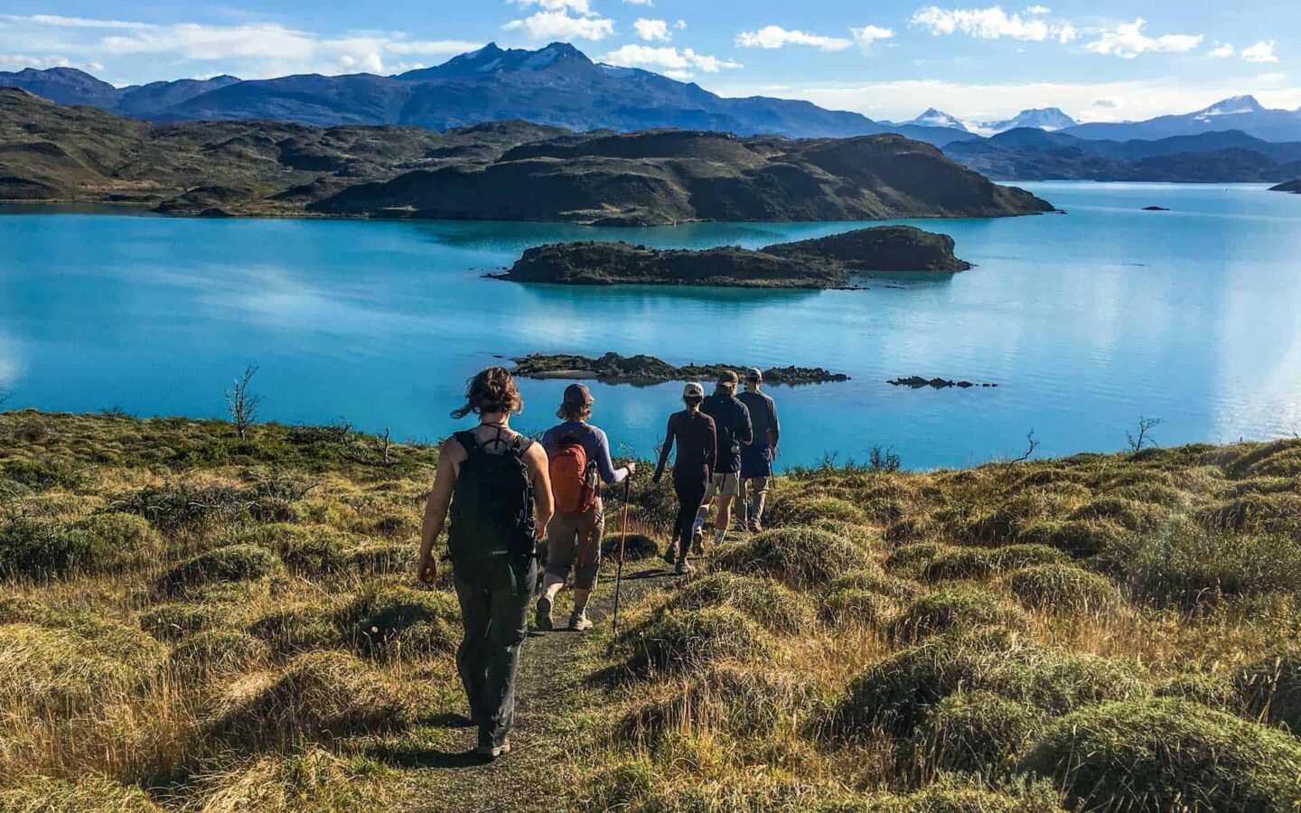 Group of hikers walking on a trail to a large turquoise lake on a sunny day during a guided trip to Patagonia