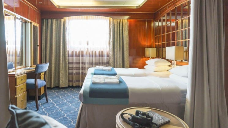 Two beds, small table, desk, chair and large window in Classic Suite aboard Sea Spirit small ship