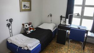 Room with bed, desk, chair, window at Hotel Angmagssalik in East Greenland