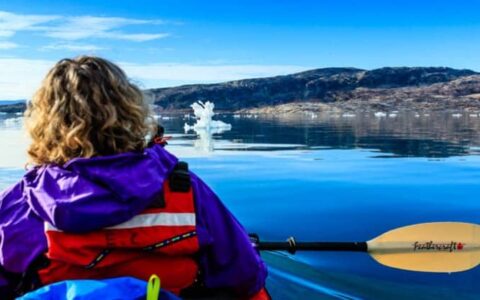 Up close of a female kayaker pausing to admire the landscape of greenland with calm waters, blue skies, and icebergs passing by