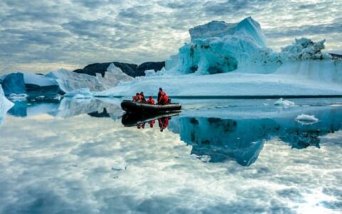 Skiff excursion with group surrounded by uniquely shaped icebergs and reflections on the still water
