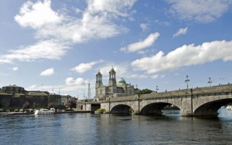 Calm, wide River Shannon running under the large stone bridge at Athlone under a sunny sky during an Ireland barge cruise.