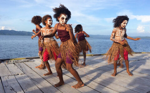 children with indigenous outfits and face paint dance on a dock on a sunny day in indonesia