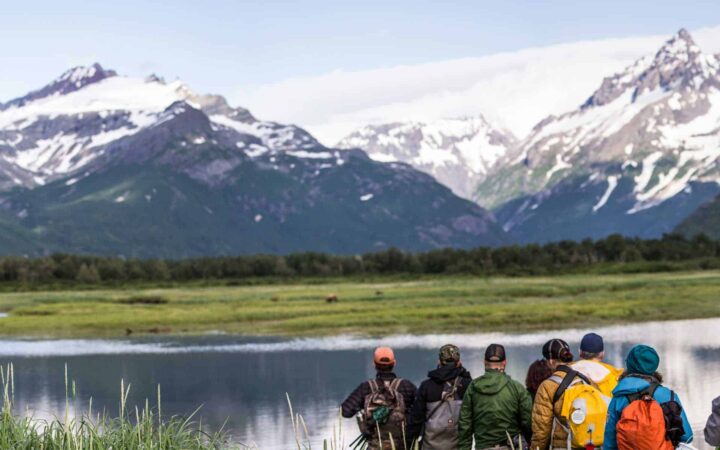 group of adventure travelers on a land tour in alaska looks at large mountains with a lake in between them