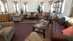 White-walled yurt with tall windows, house plants, coffee table, carpets & couches at Base Camp Greenland.