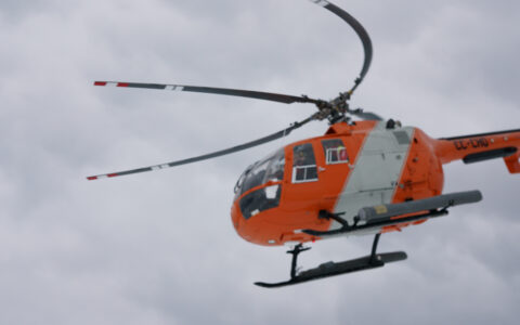 Orange & white helicopter flies among white clouds in Antarctica during the Bellingshausen Sea Cruise with Helicopters.