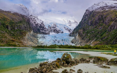 Adventurist exploring the glaciers of Patagonia next to teal water and steep green mountains