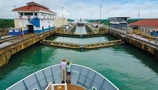 two travelers on the bow of the national geographic quest small ship about to go into the panama canal on a partly sunny day