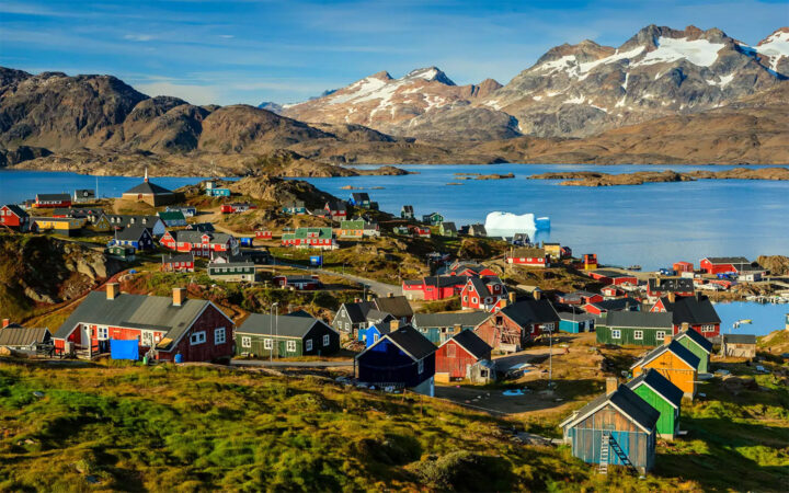 Green flash of the northern lights seen in a dark blue sky above a small village in Greenland