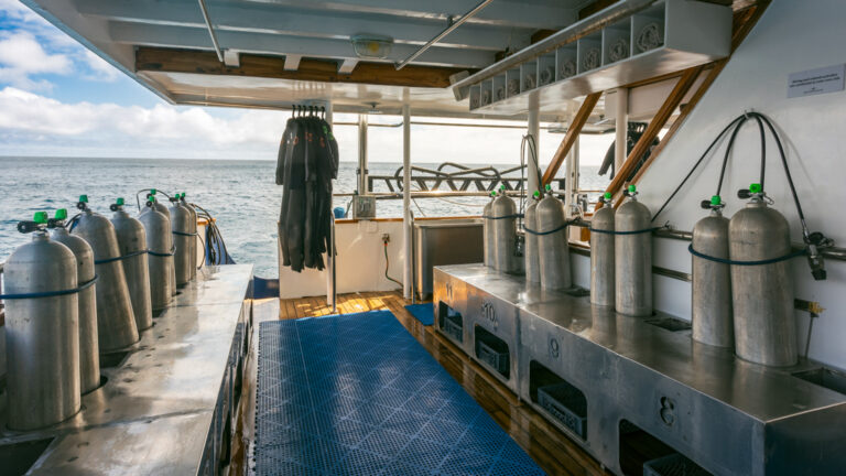 Dive deck of mv Galapagos Sky with silver oxygen tanks sitting atop metal benches with cubbies below in an open-air format.