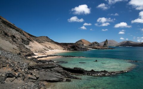 View down rocky beige hillside to turquoise water under a blue-sky day during a Galapagos Sky liveaboard dive cruise.