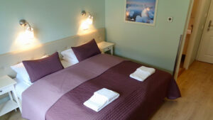 Guest room at Hali Country Hotel in Iceland with double bed in purple linens, wood floor, reading lamps & mint green walls.