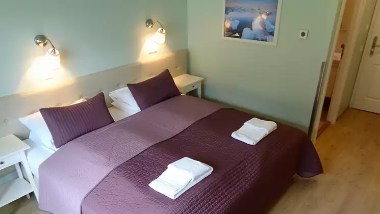 Guest room at Hali Country Hotel in Iceland with double bed in purple linens, wood floor, reading lamps & mint green walls.