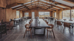 Dining room at Iceland's Highland Base Hotel with long wood banquet tables & modern chairs, high ceiling & walls of windows.