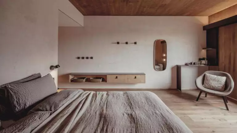 Guest room at Highland Base Hotel in Iceland with double bed in gray linens. wood floor & ceiling, natural light & modern chair.