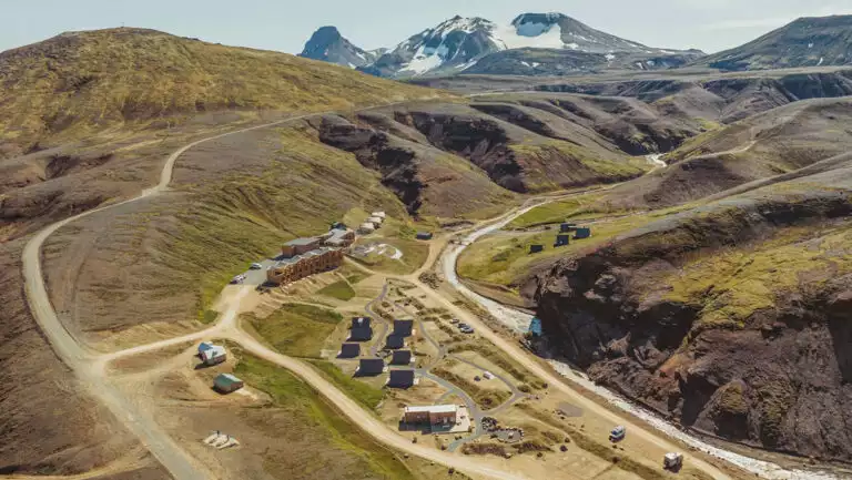 Aerial view of Highland Base Hotel in Iceland with dirt roads leading into a riverside canyon with various small buildings.