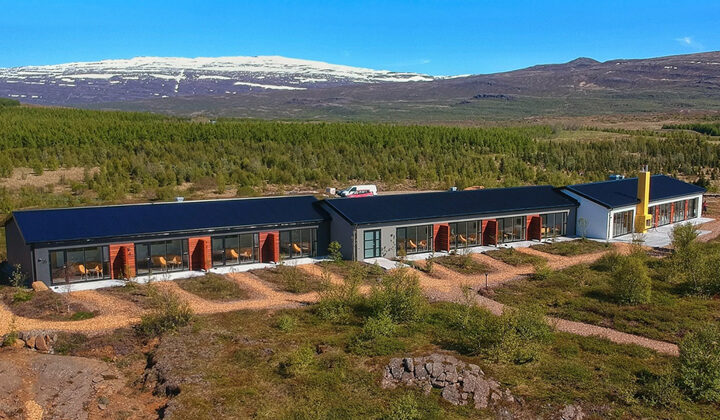 Aerial view of Hotel 1001 Nott in northeast Iceland. 1 long, modern building among green hills, with private patios & 2 hot tubs.