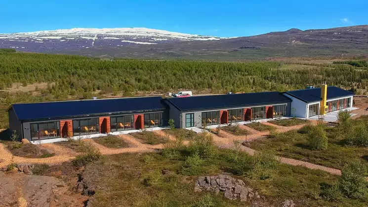 Aerial view of Hotel 1001 Nott in northeast Iceland. 1 long, modern building among green hills, with private patios & 2 hot tubs.