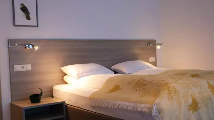 Guest room at Hotel 1001 Nott with double bed in white & yellow linens, beige wood headboard with reading lights & bedside table.