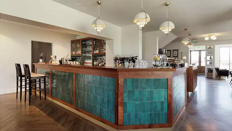 Bar of Hotel Budir in Iceland with teal tiles & wood edges, modern stools, pendant lighting, wood floors & open space.
