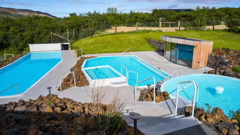 Manmade pools show teal among bright green grass on a sunny day at Iceland's Hotel Husafell.