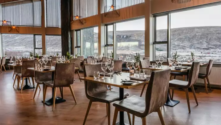 Restaurant at Hotel Husafell in Iceland with 2 stories of large windows, modern leather chairs, wood floors & 2- & 4-top tables.