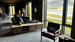 Lounge area at Hotel Jokulsarlon in Iceland with minimalist leather seats & couches, wood tables & view windows to green field.