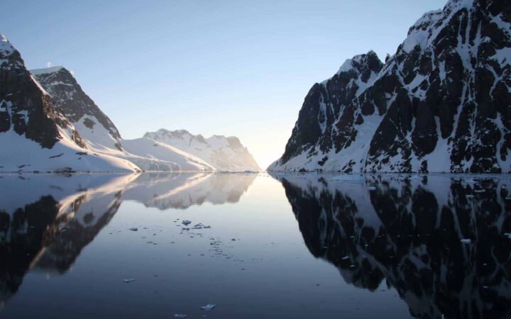 looking down a serene passage in antarctica on a sunny day with large mountains on either side and in the distance
