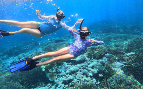 Mother & daughter snorkel in blue sea above colorful corals on a Jewels of Raja Ampat Indonesia sailing cruise.