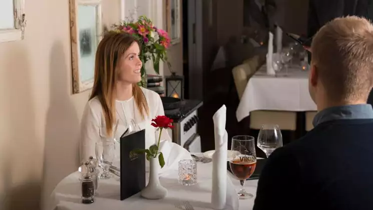Young woman & man sit down to dinner at fine dining restaurant with white tablecloth at Lake Hotel Egilsstadir in Iceland.