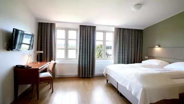 Guest room at Lake Hotel Egilsstadir with double bed in white linens, wood desk, flatscreen TV, green decor & sunny windows.