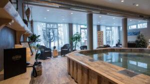Spa room with wood floors, empty hot tub & walls of windows at Lake Hotel Egilsstadir in Iceland.