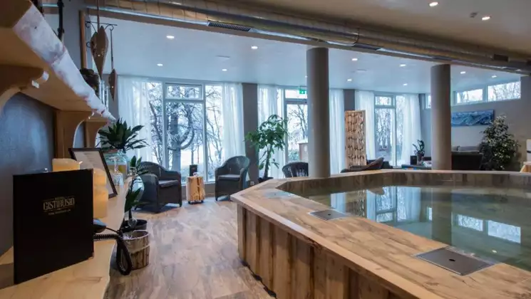 Spa room with wood floors, empty hot tub & walls of windows at Lake Hotel Egilsstadir in Iceland.