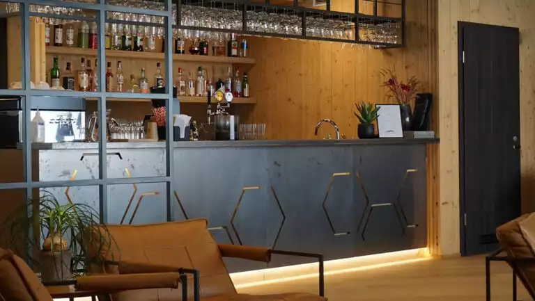 Bar at Landhotel in Iceland with hexagons cut into black metal facade, accent lighting, wood floor & modern brown leather chairs.
