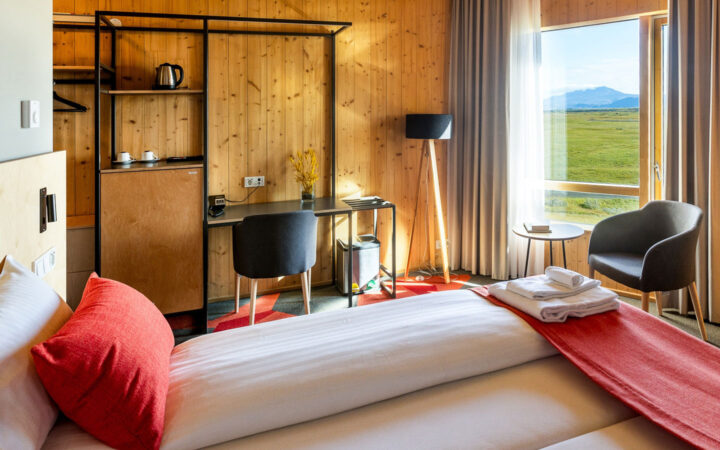 Cozy guest room at Landhotel in Iceland with 2 joined twin beds, wood walls, desk & floor-to-ceiling window to green hills.