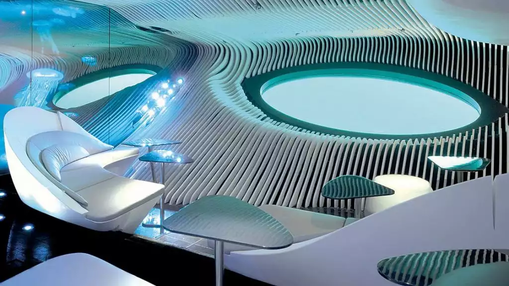Blue Eye underwater lounge on Le Dumont D'Urville French ship, with wave-like designs, white leather rounded sofas, whale's eye windows & small tables, all in blue & turquoise colors.