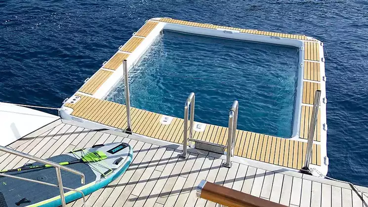 Saltwater pool barrier on back of Le Ponant cruise ship with wraparound teak deck & stand-up paddleboard sitting on deck nearby.