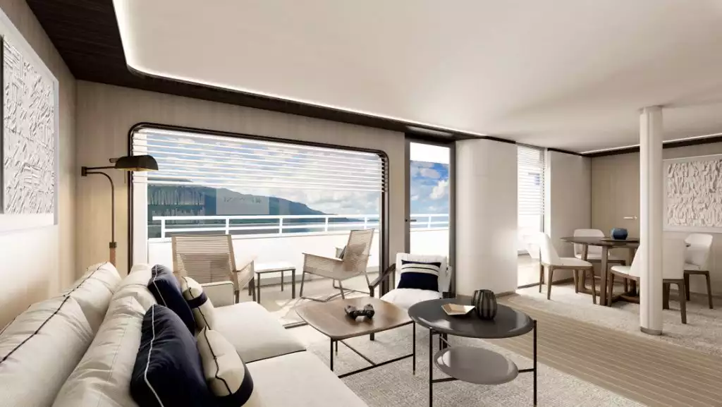 Cabin living room on Le Ponant ship with small beige couch, coffee tables, dining table & 4 chairs & glass door to balcony.