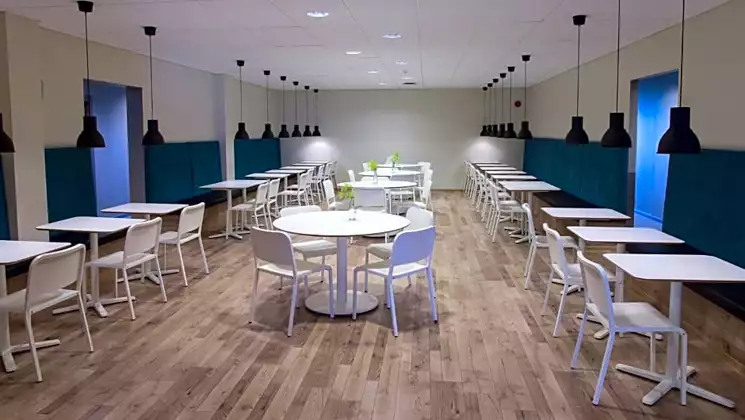 Dining room at Milk Factory Iceland with wood floor, white metal tables & chairs, dark pendant lights & teal velvet benches.