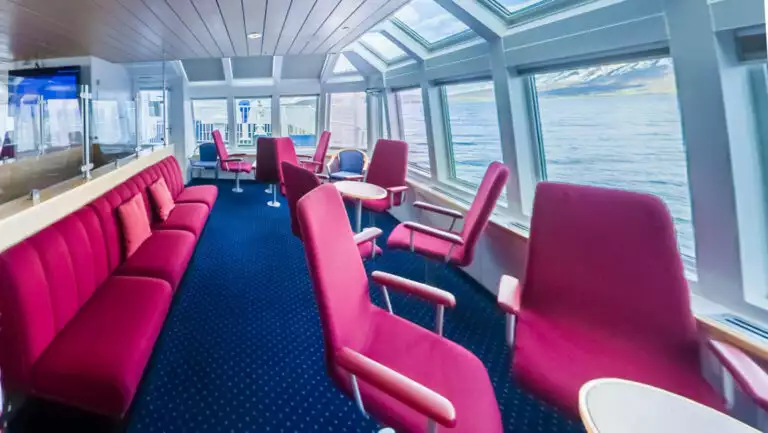 Panorama Lounge on Ocean Nova expedition ship with walls of view windows, tall red seats & benches, small tables & blue carpet.