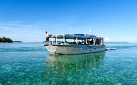 Xplorer tender vessel with silver hull & open-air, shaded seating area motors through turquoise sea in Indonesia.