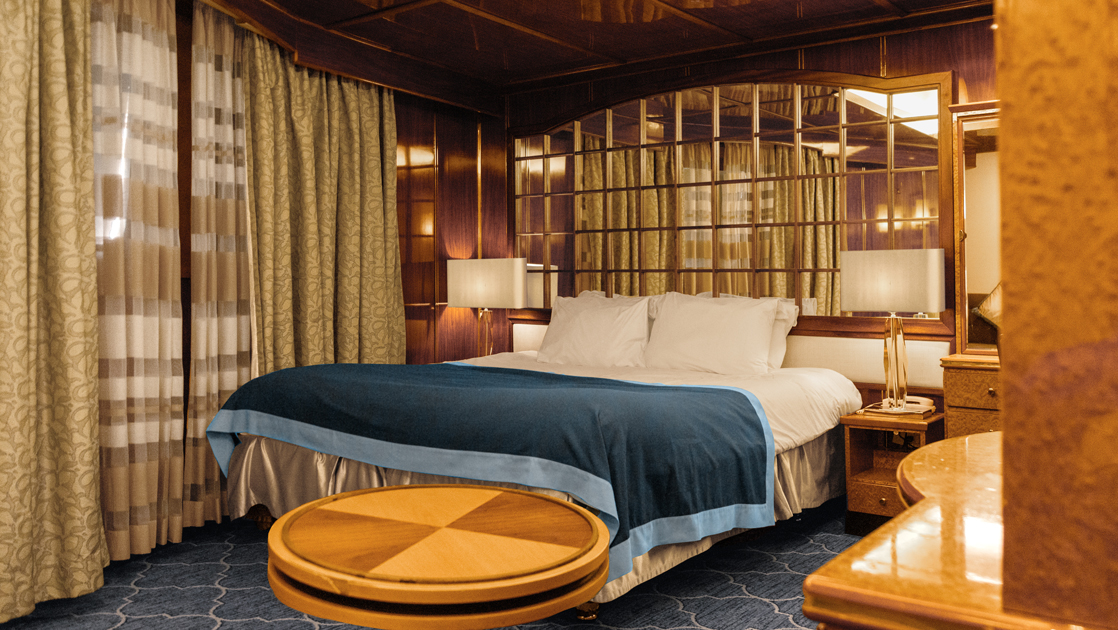 King-size bed in Single Suite on Sea Spirit polar ship with mirrored headboard, picture window & wood accents.